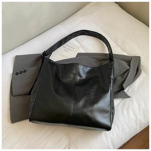 Close-up of black PU leather shoulder bag with pleated texture on grey suit