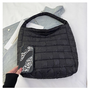 Detail of black quilted puffer tote bag showing textured square padding and wide strap