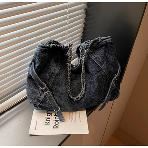 Detailed view of dark blue washed denim shoulder bag with metal chain strap and drawstring
