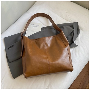 Close-up of brown textured leather hobo bag on white cloth with blazer and book