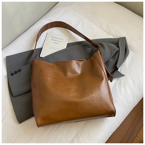 Detail of vintage brown leather tote bag with wide strap on grey blazer with a book