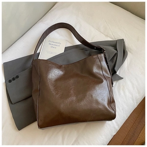 Detail of dark brown leather tote bag with glossy wrinkled texture on white backdrop
