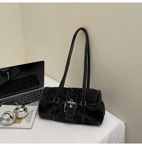 Détail du sac bandoulière en denim noir lavé avec boucles sur un bureau minimaliste