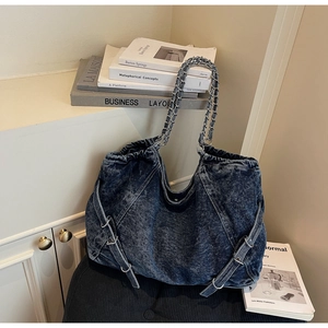 Detail of washed denim tote with metal chain straps and side buckles on white background