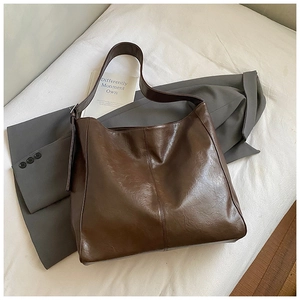 Detailed close-up of dark brown glossy leather tote bag on a grey blazer sleeve