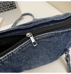 Gros plan détaillé sur la fermeture éclair argentée et le denim délavé du sac à bandoulière