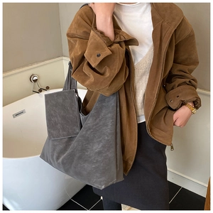 Detailed view of large grey suede tote bag with matching pouch on model in a modern room