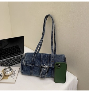 Détail du sac à épaule en jean bleu délavé avec boucle argentée sur un bureau blanc