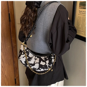 Detail of half-moon shoulder bag featuring black and white texture and gold chain strap