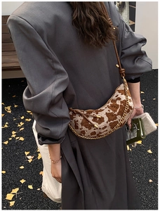 Outdoor lifestyle shot of a cow print moon bag with gold chain and autumn leaf background