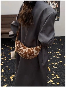 Detail of cow-print crescent bag with gold chain strap on an autumn ginkgo background