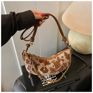 Detail of a cow print crescent bag with leather strap and gold chain on design books