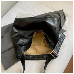 Detail of black tote bag featuring wide shoulder strap with silver eyelets and metal buckle