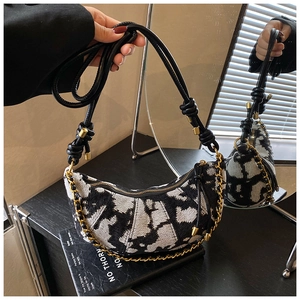 Detail of a black and white patterned crescent bag with gold chain and thin leather strap