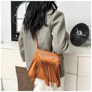 Detalle de un bolso bandolera de ante marrón con bordado bohemio y flecos largos
