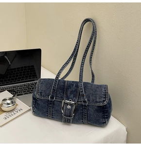 Vue détaillée du sac baguette en jean bleu foncé avec boucle argentée sur bureau blanc