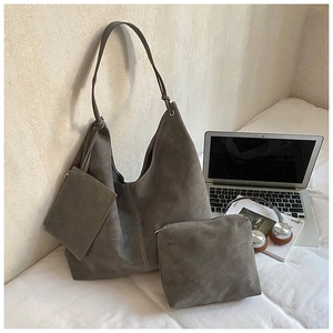 Three-piece mocha grey suede tote bag set with matching pouch and mini zipper bag on a desk