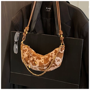 Close-up of crescent moon bag with animal print texture and gold chain on black suit