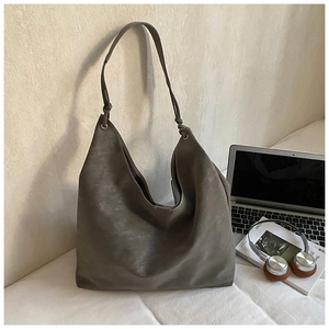 Detail of taupe oversized hobo tote with knotted strap next to laptop and headphones