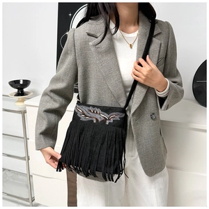 Detalle del bolso bandolera negro con flecos, bordado de hojas y textura de ante suave