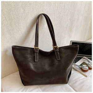 Detailopname van donkerbruine leren shopper met gouden metalen gespen en laptop op achtergrond