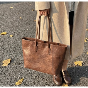Detailed close-up of dark brown vintage leather tote bag with long handles and brand logo