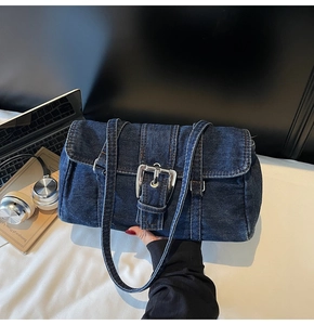 Détail d'un sac bandoulière en jean bleu avec une grande boucle en métal argenté et couture