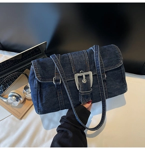 Détail d'un sac bandoulière en denim bleu foncé avec boucle argentée sur un bureau