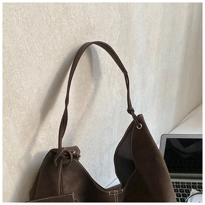 Detail of dark brown suede tote bag with white stitching and knotted drawstring shoulder strap