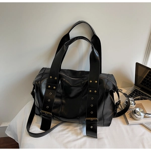 Dettaglio di una borsa tote nera con fibbie in bronzo e tracolla regolabile