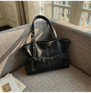 Détail d'un sac cabas en cuir noir avec surpiqûres blanches sur un canapé gris
