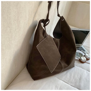 Detail of a dark brown large tote bag with white contrast stitching on a bed