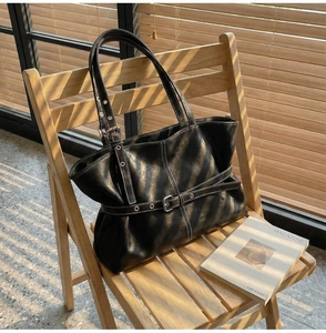 Détail d'un sac cabas vintage en cuir noir avec boucles sur une chaise en bois