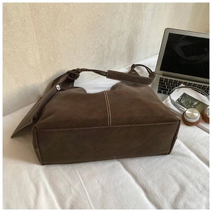 Detail view of large brown tote bag with contrast stitching and small pouch on white texture