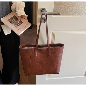 Close-up of retro brown leather tote bag hanging on a door with textured finish