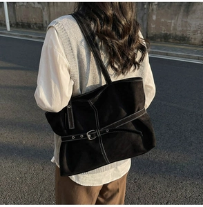 Détail d'un sac cabas noir avec surpiqûres blanches et ceinture à boucle métallique