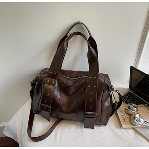 Dettaglio di una borsa tote grande in finta pelle marrone scuro con borchie e accessori per PC
