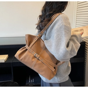 Détail d'un sac cabas en cuir caramel avec plis et boucles porté sur un pull en maille