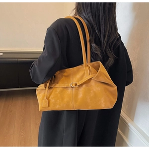 Detalle de un bolso tote de cuero amarillo jengibre llevado por una modelo con blazer negro