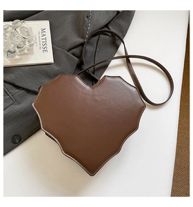 Detailansicht der herzförmigen braunen Ledertasche mit weißen Nähten auf dem Tisch