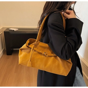 Vista lateral de un bolso tote amarillo con pliegues y hebilla sobre un blazer negro