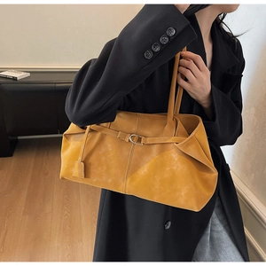 Detalle de un bolso tote de cuero sintético amarillo mostaza con hebilla en blazer negro
