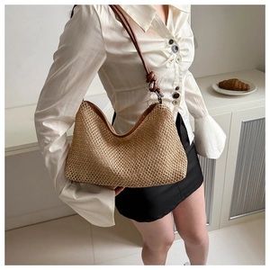 Détail du sac cabas en paille tressée beige avec nœuds en cuir marron sur un mannequin