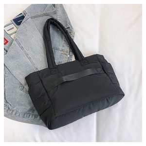 Detail of black quilted nylon tote bag with reinforced strap shown on denim jacket