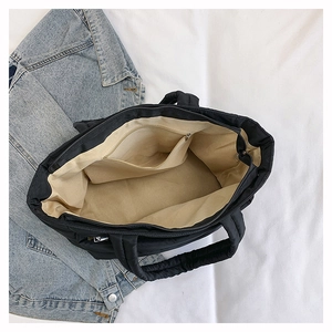 Internal view of black quilted tote bag showing spacious beige lining and zipper pocket