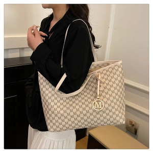 Detail of a large beige tote bag with M-pattern print and a gold metallic charm