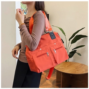 Détail d'un grand sac cabas orange en nylon avec poches zippées porté par un mannequin