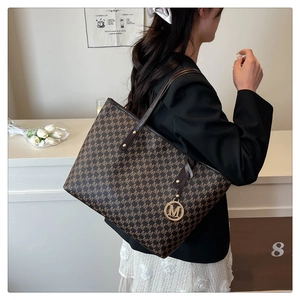 Detail view of large tote bag with brown M-letter print and round metal logo charm