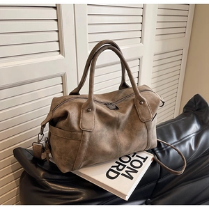 Close-up of vintage taupe leather boston bag with metal zippers on a leather sofa