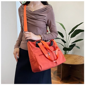 Sac fourre-tout orange en nylon porté par un mannequin dans un cadre domestique cosy